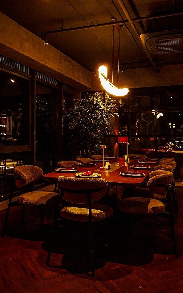 A dimly lit restaurant dining room with set tables and a curved pendant light overhead